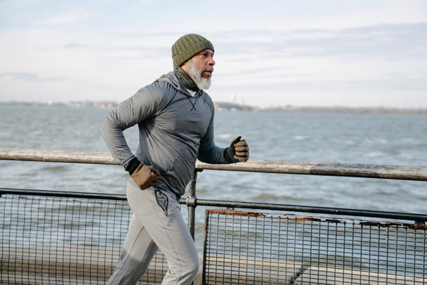 A fit older man runs outdoors while wearing fitness gear.