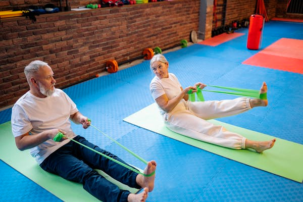 Two people in a workout class use resistance bands to assist themselves during exercise.